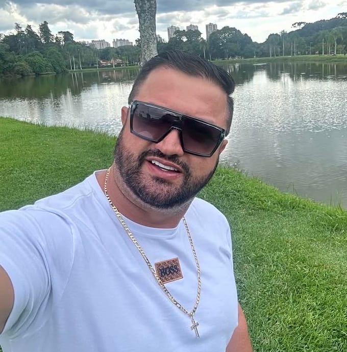 José Elias Lopes, proprietário da Mecânica Lopes, sorrindo de óculos escuros à beira de um lago